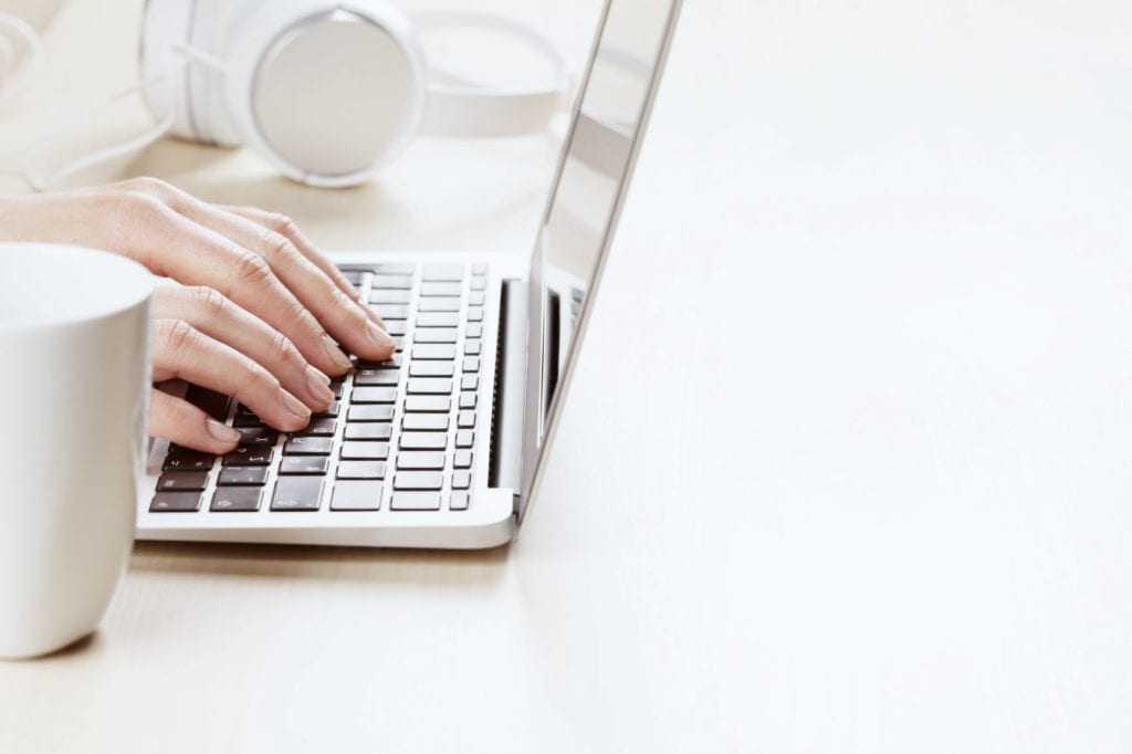 A close-up shot of a person's hands typing on a laptop keyboard with precise hands and a white desk space