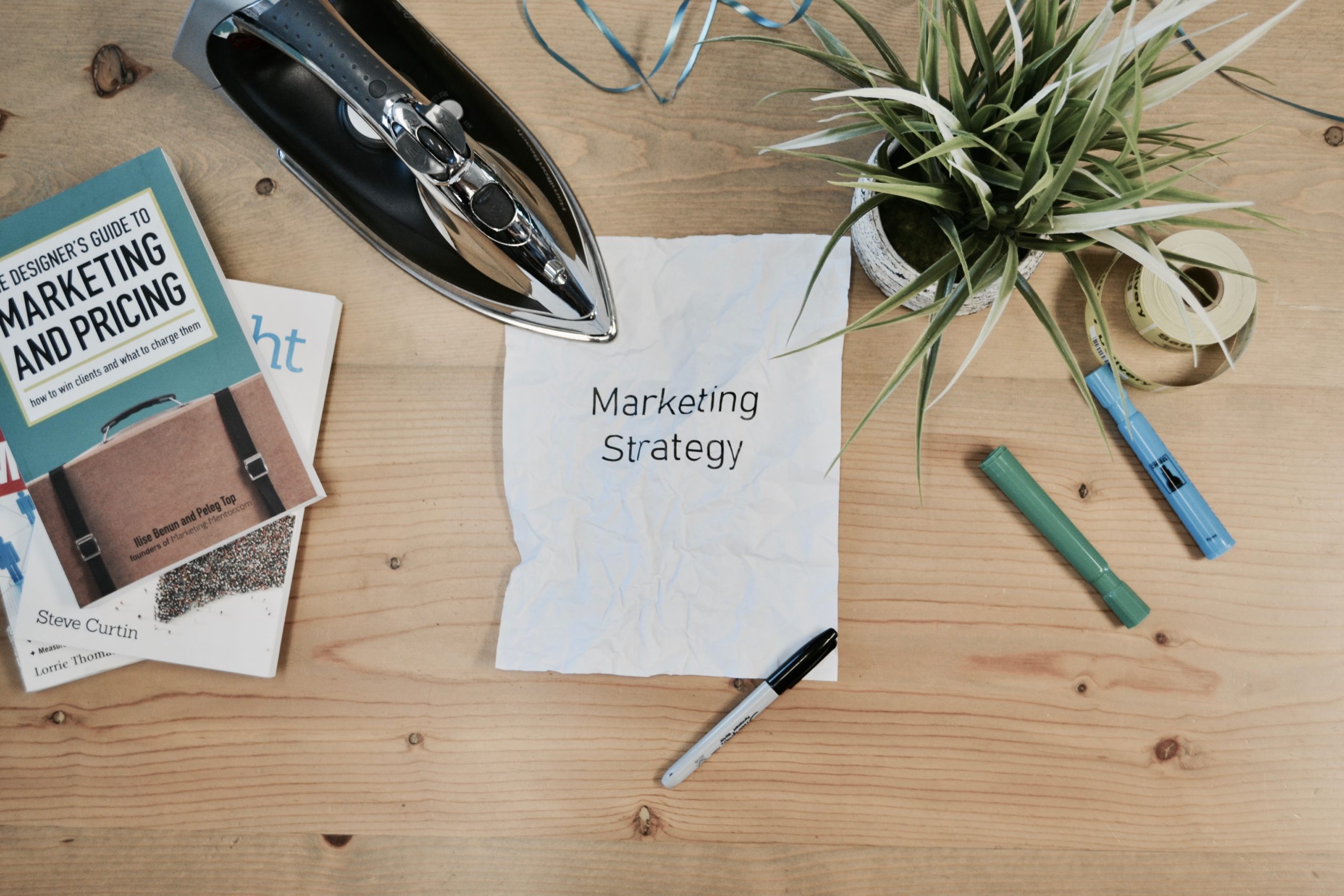 A desk with highlighters, books, a plant, and a crumpled paper with a marketing strategy text