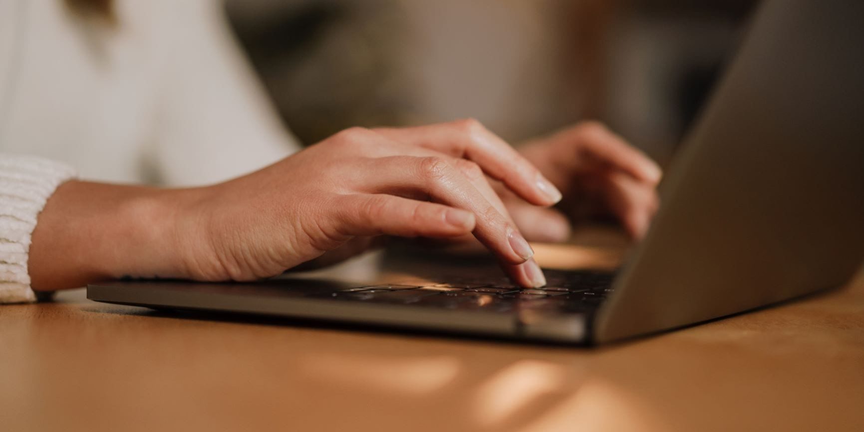A close-up of the person's hands typing on a laptop keyboard, with only a tiny portion of the person's wrist visible in the frame