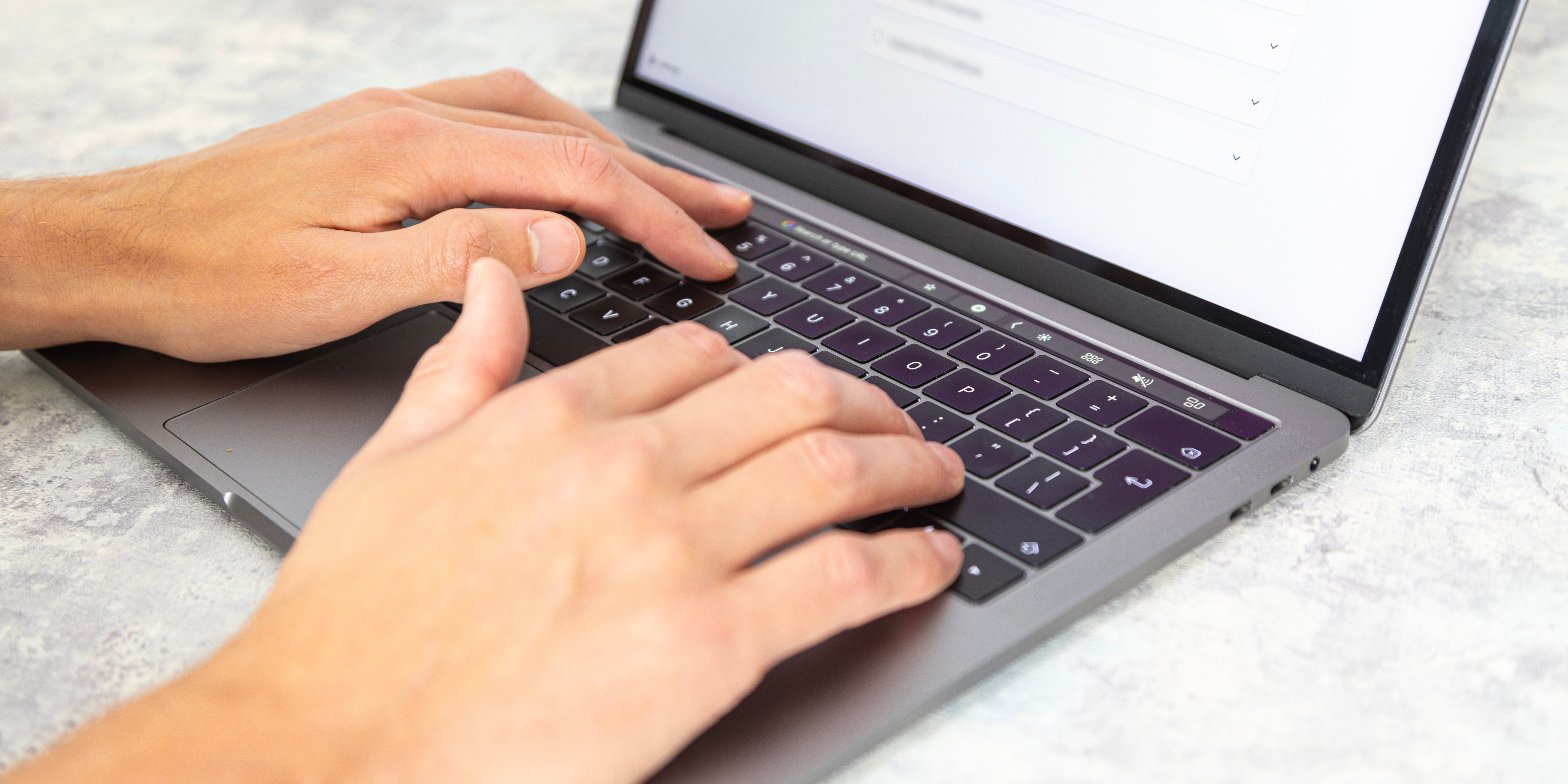 A close-up of a man's hands typing on a laptop keyboard